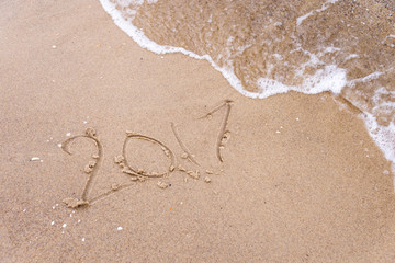 Inscription written in the wet beach sand being washed with sea water wave. Time passing away or New Year celebrating concept.