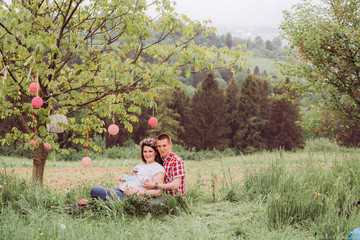 Pregnant woman in blue jeans and a T-shirt with her husband on the mountains background. Future parents