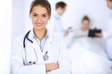 Female doctor smiling on the background with patient in the bed and two doctors