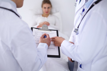 A group of doctors discussing medical history close up , a happy smiling patient in the background.