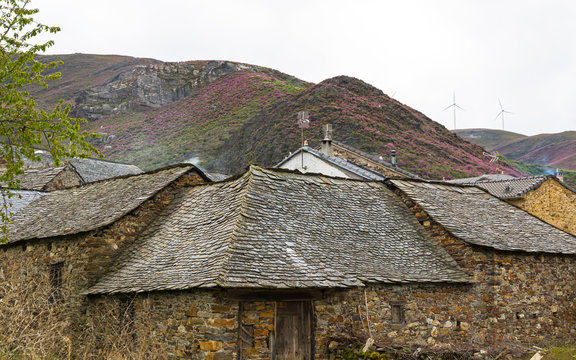 Construcciones Rurales en Pueblo de Monta&ntilde;a -  Casas tradicionales en piedra con tejados de pizarra en paisaje monta&ntilde;oso con vegetacion de primavera. Con aerogeneradores en lo alto de una colina