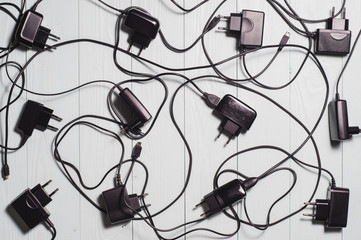 Used chargers for mobile phones on the wooden background.