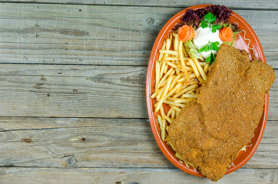 Large Wiener Schnitzel on a clay plate with fries