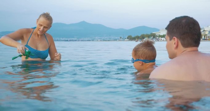 Young parents and little son bathing in the sea. Mom and child playing with windup frog. Family summer vacation