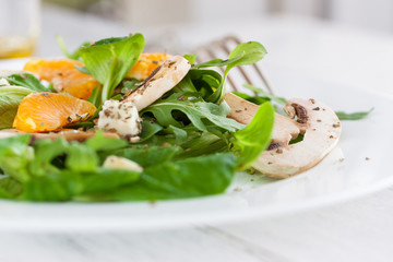 Sommer salad with rocket salad, mandarin, mushrooms and cheese gorgonzola in a white ceramic bowl , closeup.