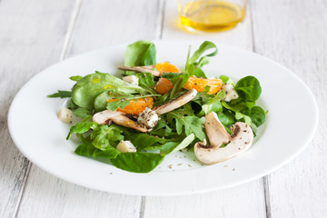 Sommer salad with rocket salad, mandarin, mushrooms and cheese gorgonzola in a white ceramic bowl , closeup..