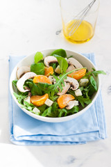 Sommer salad with rocket salad, mandarin, mushrooms and cheese gorgonzola in a white ceramic bowl , closeup..