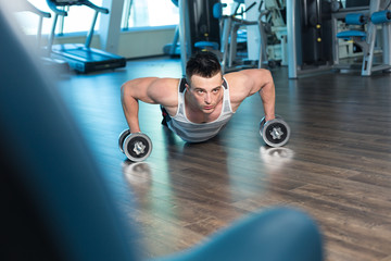 Fototapeta na wymiar Muscular man doing push-ups on dumbbells in gym. Powerful male e
