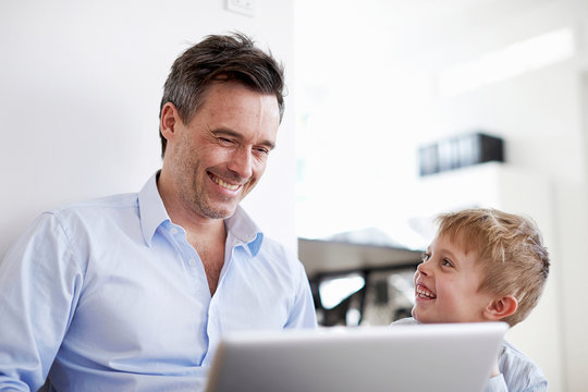 Man using laptop, son watching