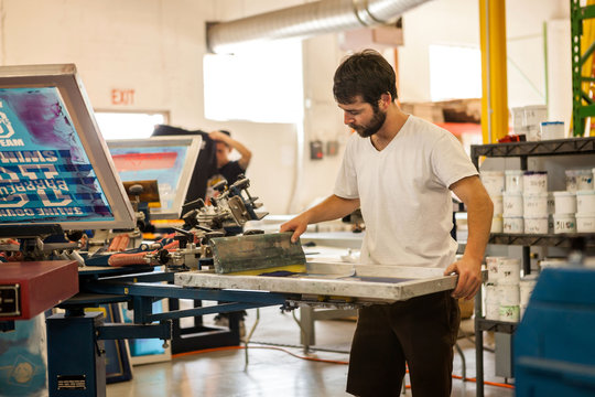 Worker pressing ink on frame in screen printing workshop