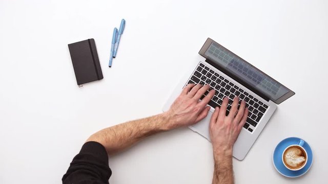 Man types on a laptop on his desk with coffee . Upview