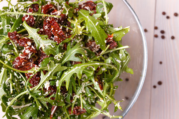 Green healthy salad with arugula and sun-dried tomatoes and parmesan cheese on a wooden kitchen table. Pepper and seasonings.  Italian cuisine. Top view.