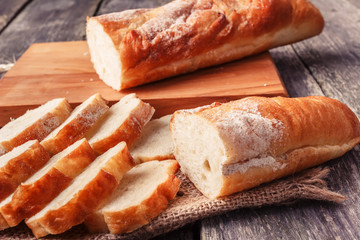 Freshly baked French baguette, sliced on a wooden board. In rustic style on sackcloth.