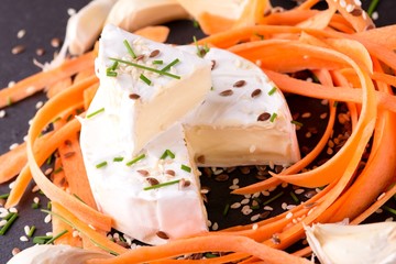 Portion of camembert cheese with carrot and healthy seeds