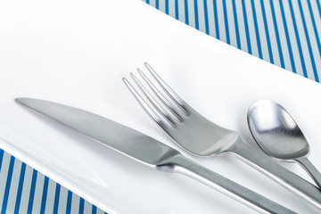 Geschirr, Messer, Gabel und Teelöffel auf glänzender, spiegelnder, blau gestreifter...