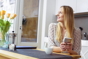 frau sitzt am küchentisch und hält ihr handy in der hand