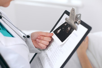 Close-up of a female doctor holding application form with ultrasonography while consulting patient