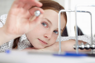 Girl playing with newton's cradle on desk