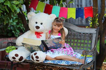 Little girl with her friend huge white bear are reading together a fairy tail book in a garden