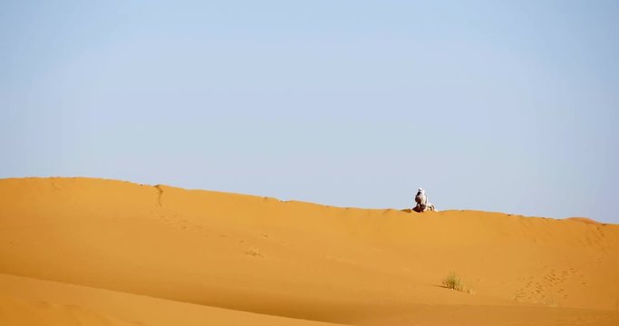 conduttore di cammelli berbero parla al cellulare seduto su una duna di sabbia nel deserto del Marocco