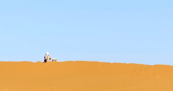 conduttore di cammelli berbero parla al cellulare seduto su una duna di sabbia nel deserto del Marocco3
