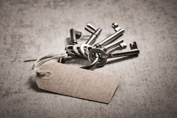 Vintage key set with blank paper tag on stone table. Symbol of nostalgia, security and access.
