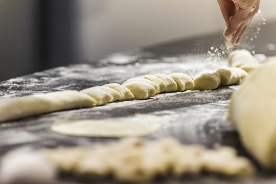 Chef's hand sprinkling flour on gnocchi in commercial kitchen