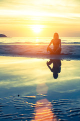 Female silhouette with reflection in water, meditation pose at sunset.