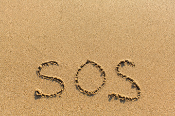 SOS - written manually on the texture of sea sand.