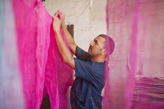 Man hanging up dyed fabric in traditional milliners workshop