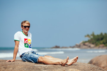 Attractive young sexy man sitting on a rock near the sea