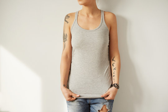 Woman wearing grey blank sleeveless t-shirt. Home wall background.