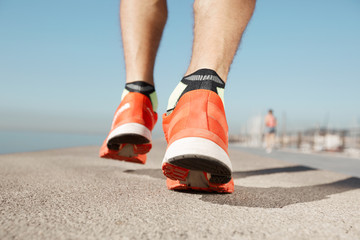 Athlete runner feet running on road closeup on shoe. Man fitness jog workout wellness concept. Man runner legs and shoes in action on road outdoors at road near sea.