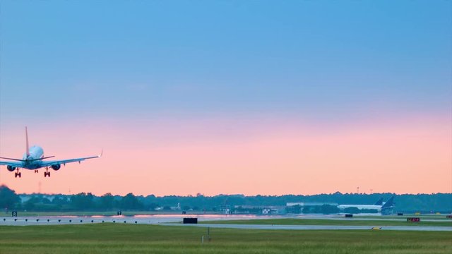 Air Travel Scene at an Airport with a Landing Commercial Passenger Airplane onto a Runway featuring a Vibrant Colored Sky with Blue, Orange and Pink Colors during Sunset