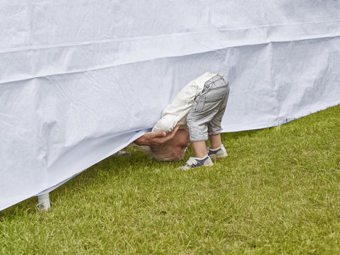 Young boy bending forward to reach fathers hand under tent