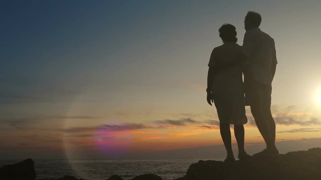 Couple stands on the cliff overlooking the sea at sunset time