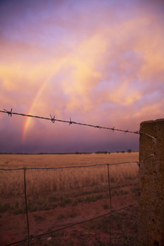 View of wire fence, rainbow and storm clouds at sunset, Ultima, Victoria, Australia