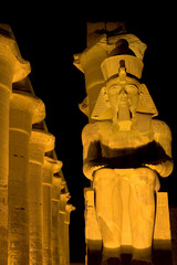 Egypt. Illuminated Luxor Temple. Granite statue of Ramesses II and the processional colonnade of Amenhotep III