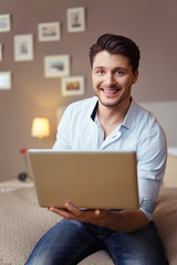 mann sitzt auf dem bett und hält laptop in der hand