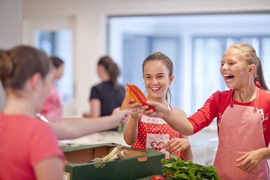 Teenage girls holding up chillies and carrot in kitchen
