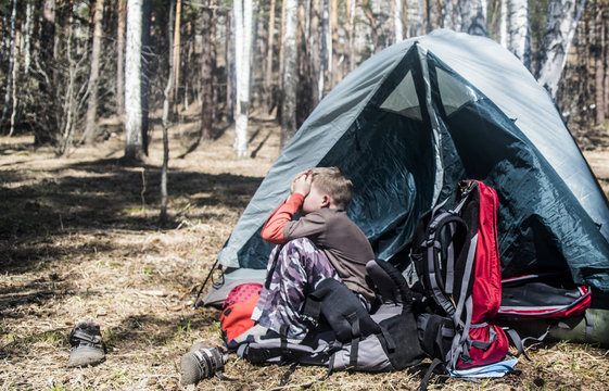 Boy with hands over his face sitting outside tent in forest