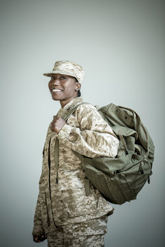 Side view studio portrait of confident female soldier with rucksack