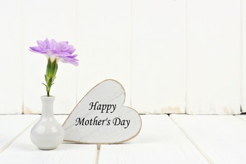 Happy Mother's Day heart tag with small vase and single purple carnation flower against a white...