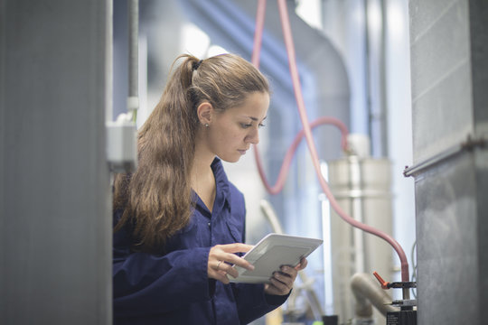 Female engineer checking factory machinery using digital tablet