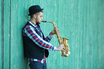 Young man playing on saxophone outside near the old wall
