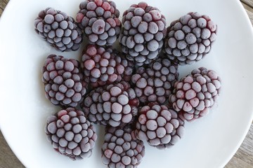 Frozen blackberries on a white plate. Closeup