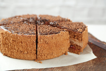 Sliced chocolate cake on wooden table, on light background