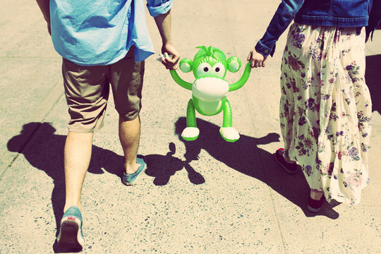 Cropped rear view of couple holding hands with inflatable monkey