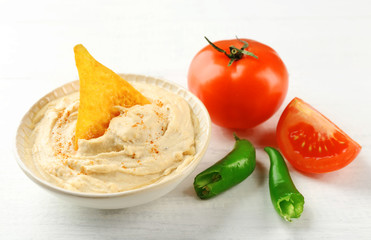 Ceramic bowl of tasty hummus with chips, chili and tomato on table
