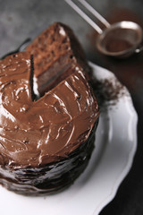 Chocolate cake on plate with a cut piece and fork and cocoa on gray background, closeup